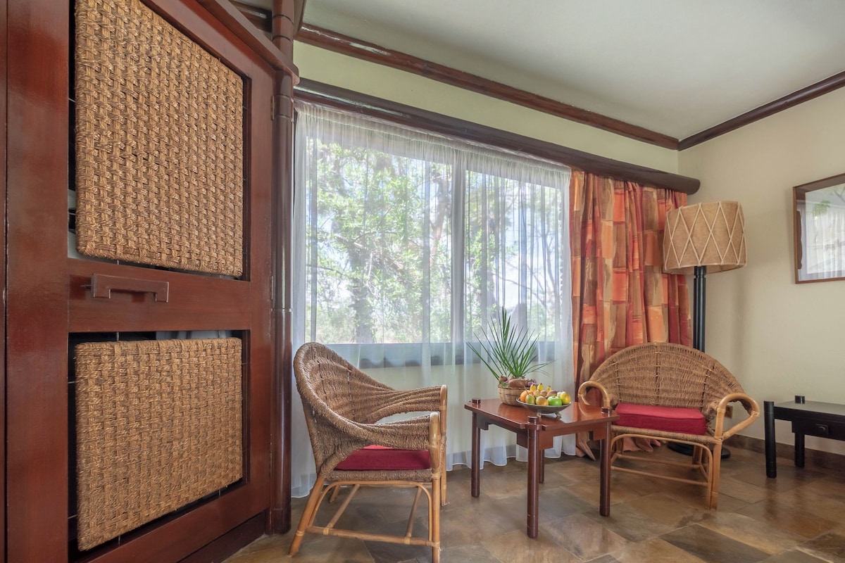 A room with two wicker chairs, a table with a fruit bowl, and a lamp.