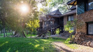 A rustic building with a stone facade, wooden staircase, and a tree-lined yard.