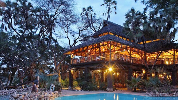 A resort with a pool, wooden structures, and palm trees.