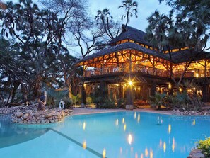 A resort with a pool, wooden structures, and palm trees. - Sarova Shaba Game Lodge (Archers Post)