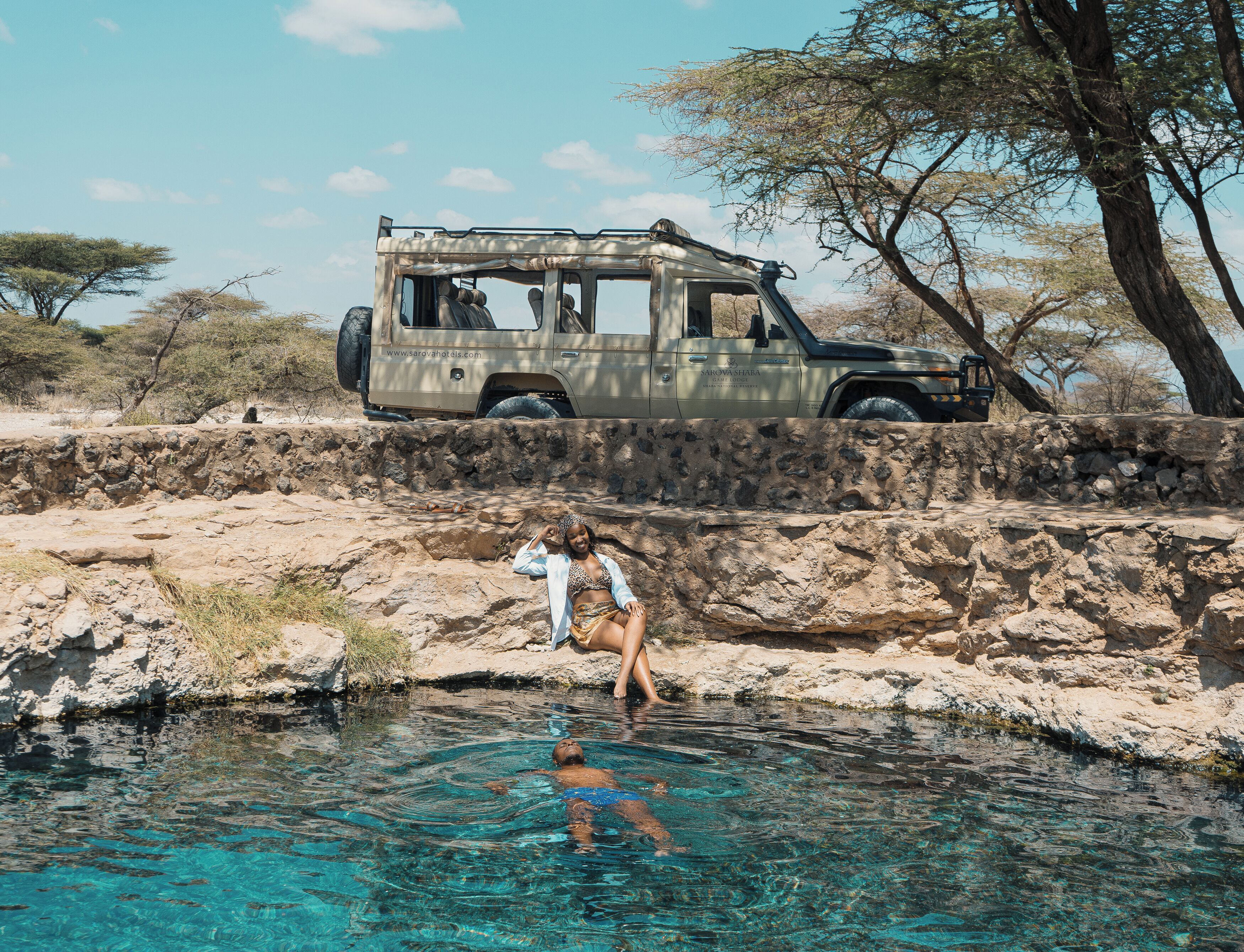 Un jeep estacionado sobre terreno rocoso con una piscina clara al frente.