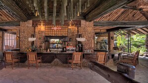 An outdoor bar area with stone walls, wooden furniture, and a rustic ceiling.