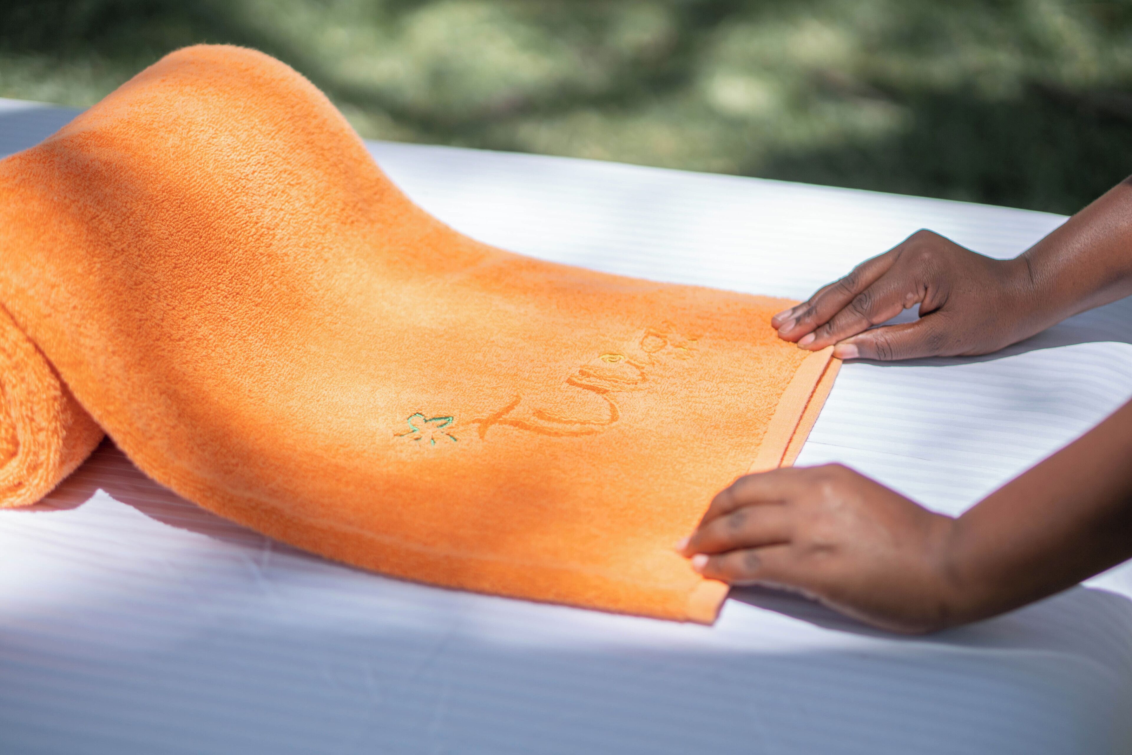 A person placing an orange towel on a bed.