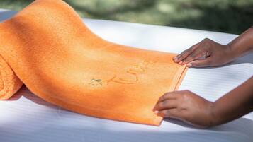 A person placing an orange towel on a bed.