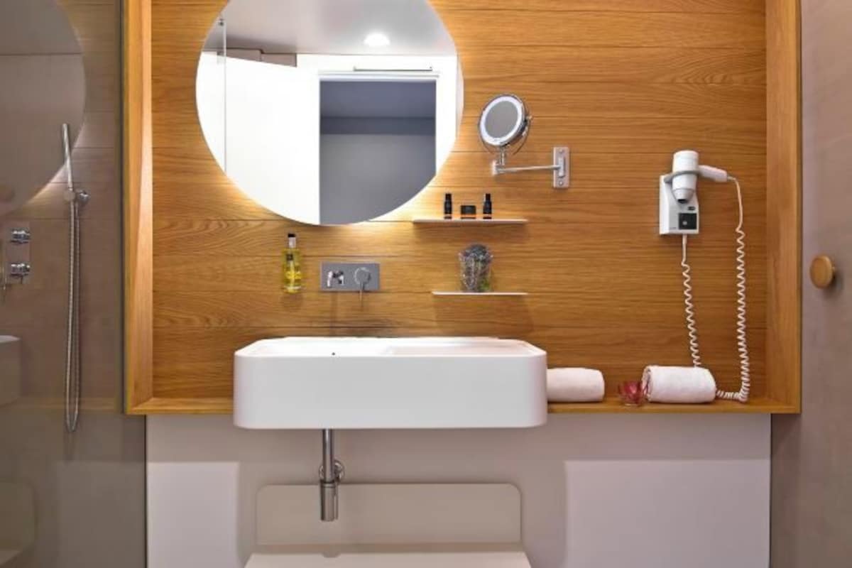 A bathroom with a wooden vanity, a sink, a mirror, a hairdryer, and a towel rack.