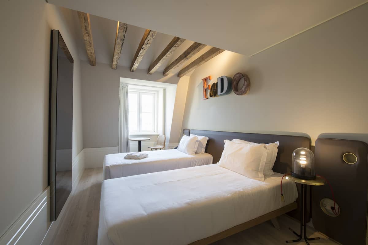Une chambre d’hôtel avec deux lits, une petite table, une chaise et une lampe fixée au mur.