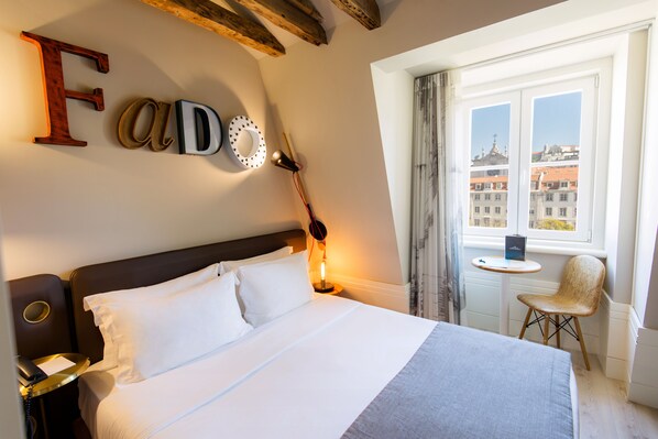 A hotel room with a bed, a desk, a chair, and a window with a view of buildings. - My Story Hotel Rossio (Lisbon)