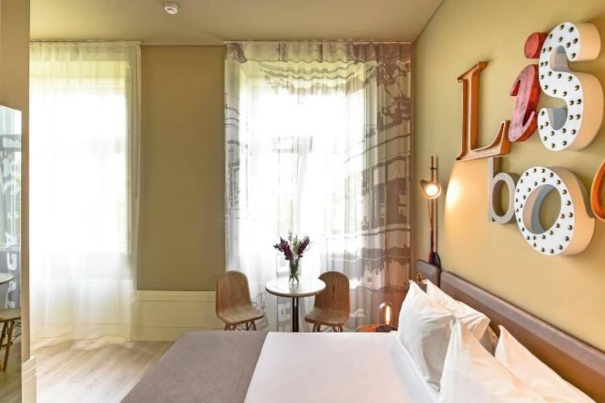 A hotel room with a bed, a small table with chairs, and a wall with decorative letters.