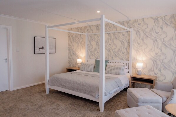Ein Schlafzimmer mit einem Himmelbett, zwei Nachttischen, einem Sessel und einem kleinen Tisch.