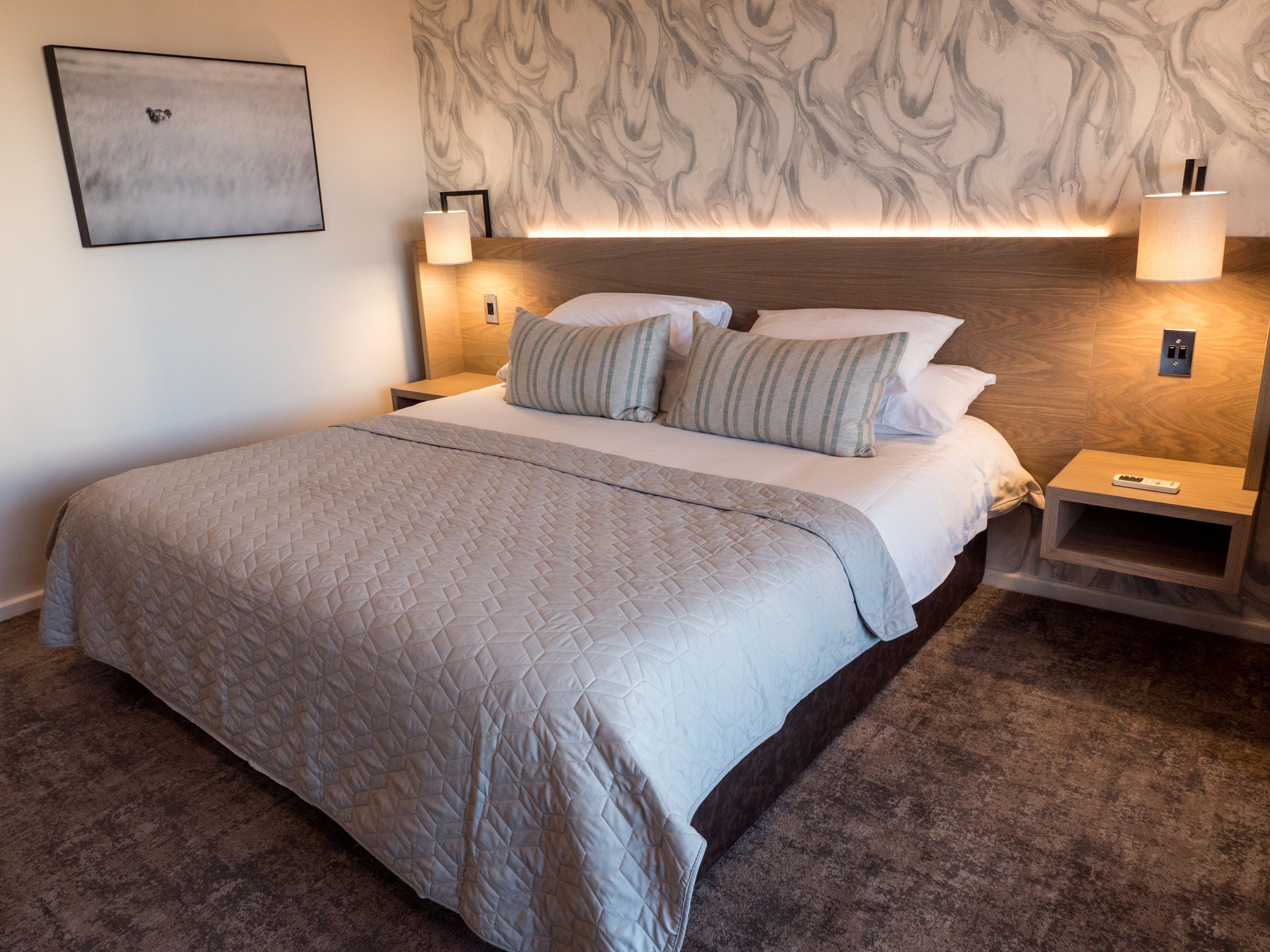 A neatly made bed with a quilted cover, two bedside lamps, and a wall-mounted picture.