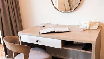 A hotel room with a wooden desk, a chair, a mirror, a telephone, and a carpeted floor.