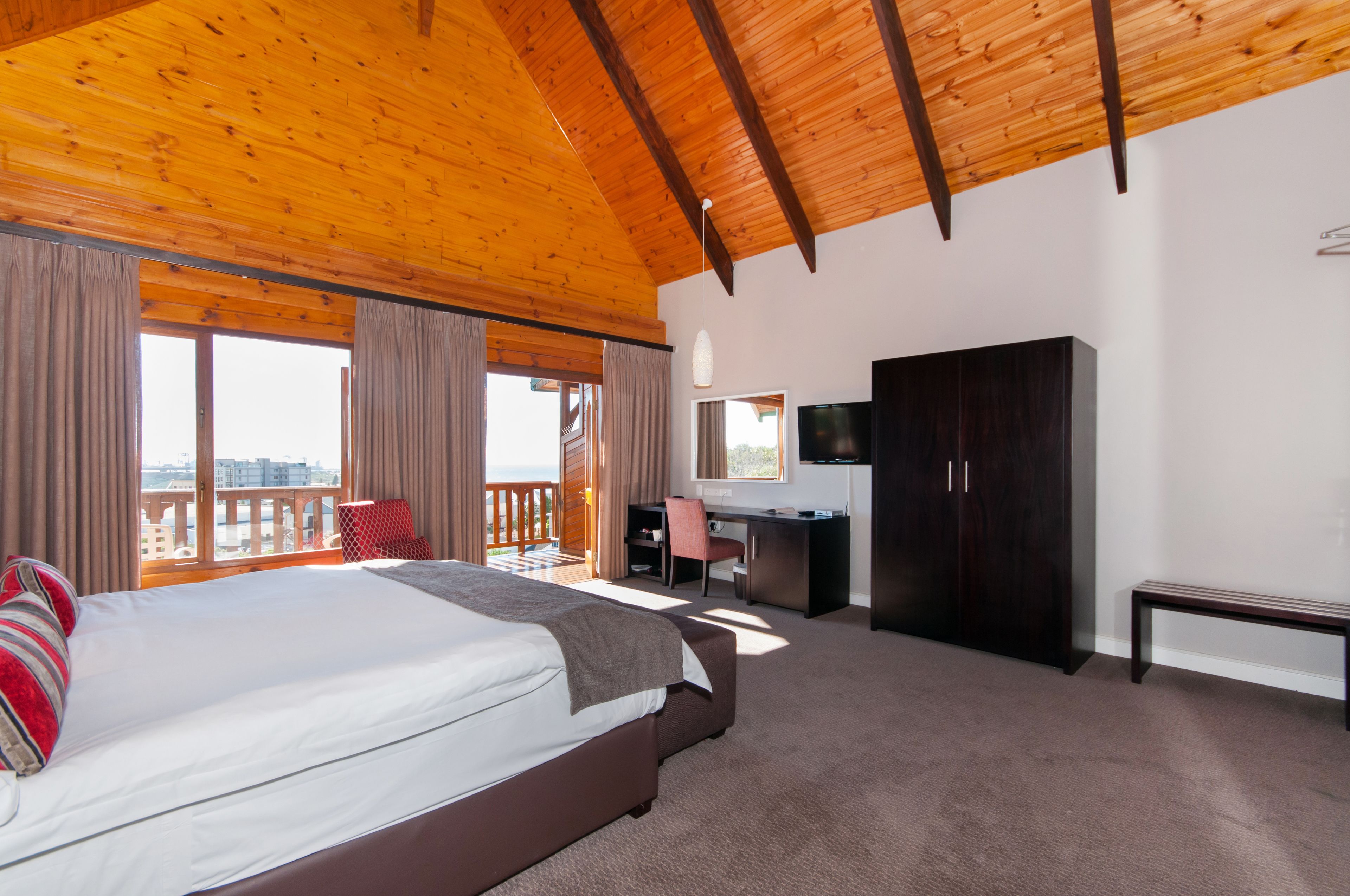 A bedroom with a large bed, a desk, a wardrobe, and a balcony with a view.