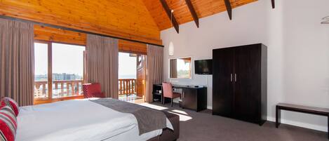 A bedroom with a large bed, a desk, a wardrobe, and a balcony with a view.