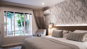 Ein Schlafzimmer mit einem großen Bett, einem Sessel, einem Fenster mit Vorhängen und einer Wand mit marmorartigem Muster.