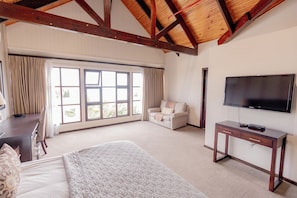 A hotel room with a bed, a desk, a chair, a sofa, a TV, and large windows.