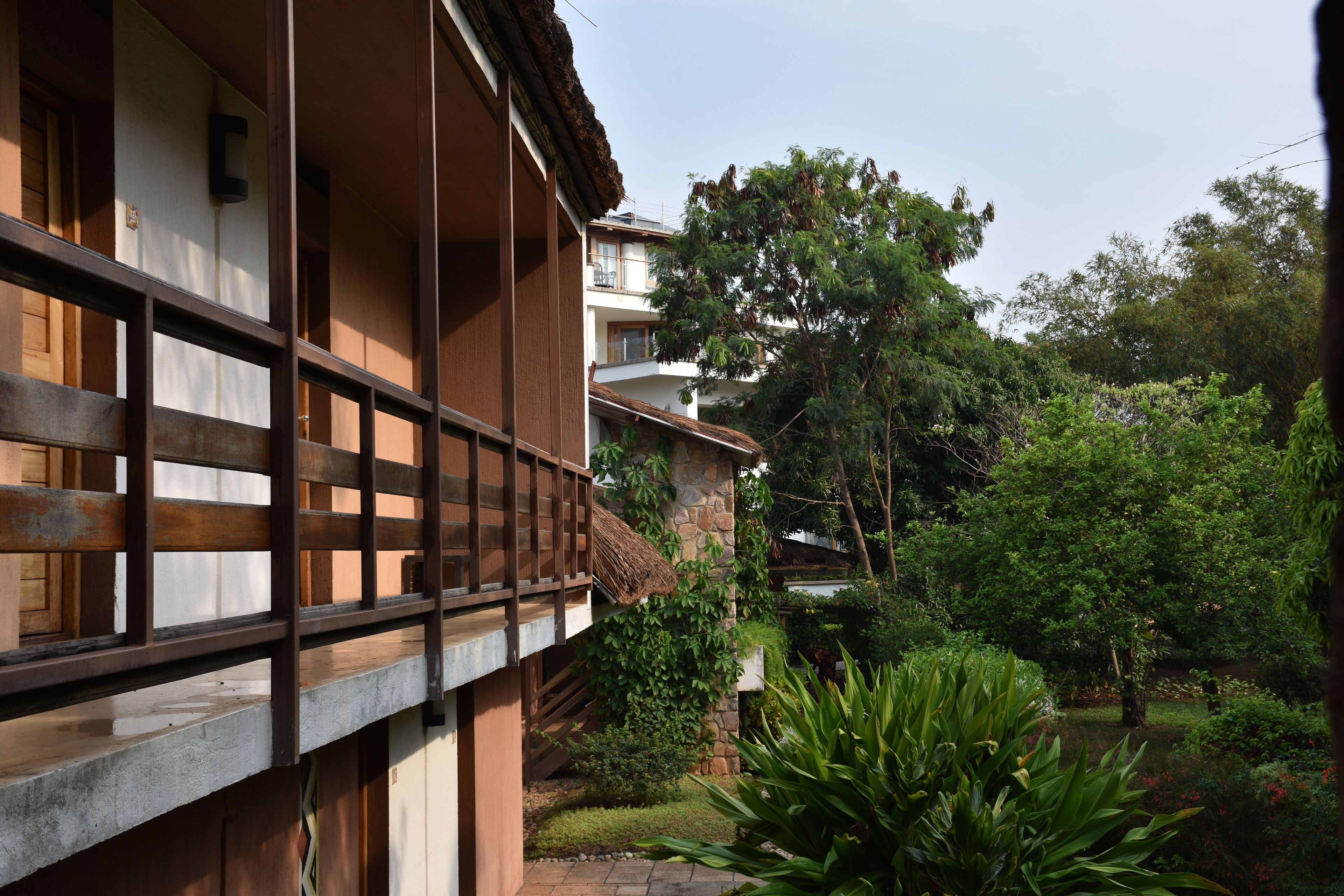 Un edificio tradicional con un balcón de madera y un jardín con diversas plantas y un estanque.