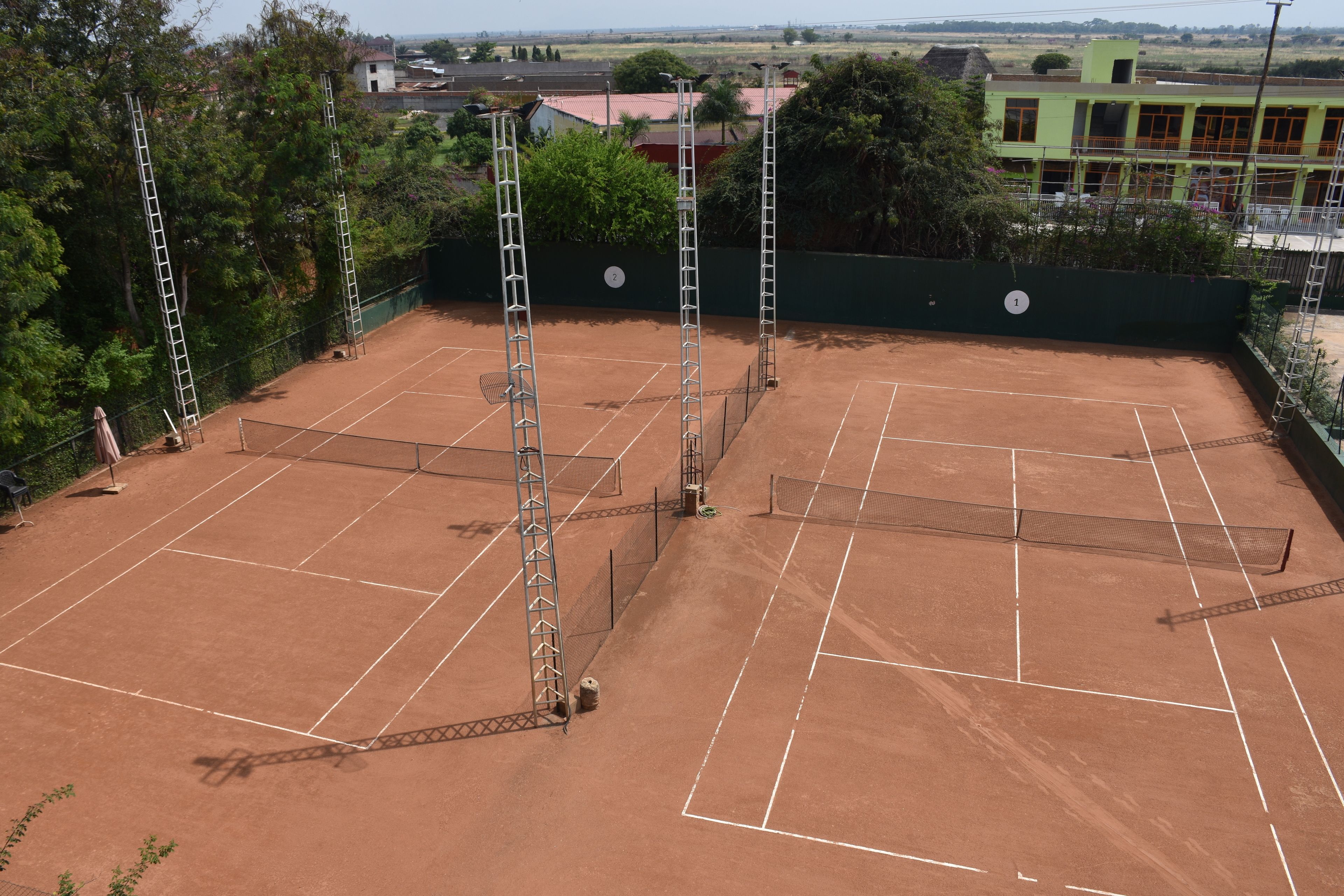 A tennis court with multiple nets and tall metal poles, surrounded by a green fence and trees.