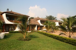 A resort with thatched-roof villas, a well-maintained lawn, and palm trees.