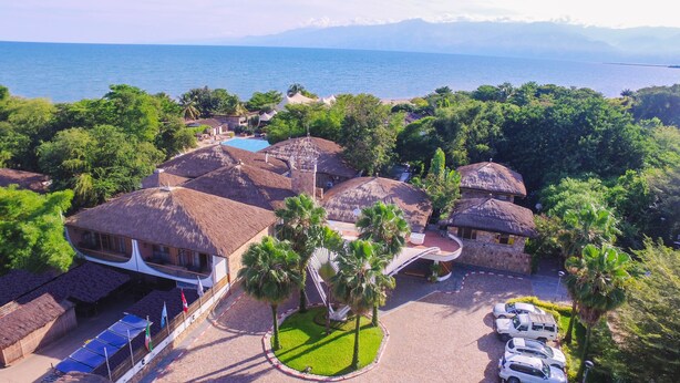 Ein Resort mit strohgedeckten Gebäuden, einem Schwimmbecken und Blick auf das Meer.