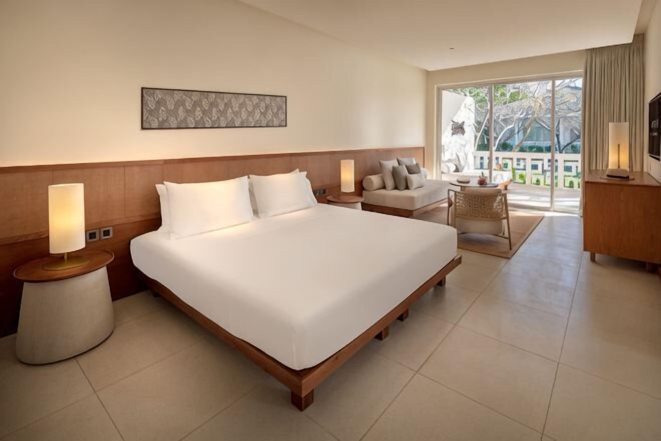 A hotel room with a large bed, bedside lamps, a sofa, a small table, and a TV.