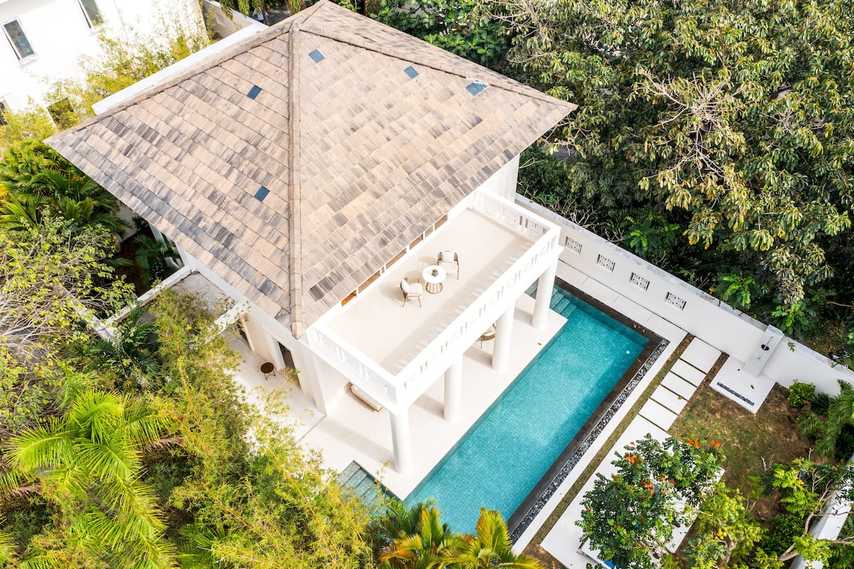 An aerial view of a house with a swimming pool, surrounded by lush greenery.