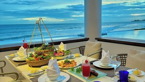 Mesa de jantar posta com pratos, talheres e uma bebida, com vista para o oceano.