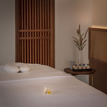 A neatly made bed with pillows, a vase with dried plants, and a small table with candles.