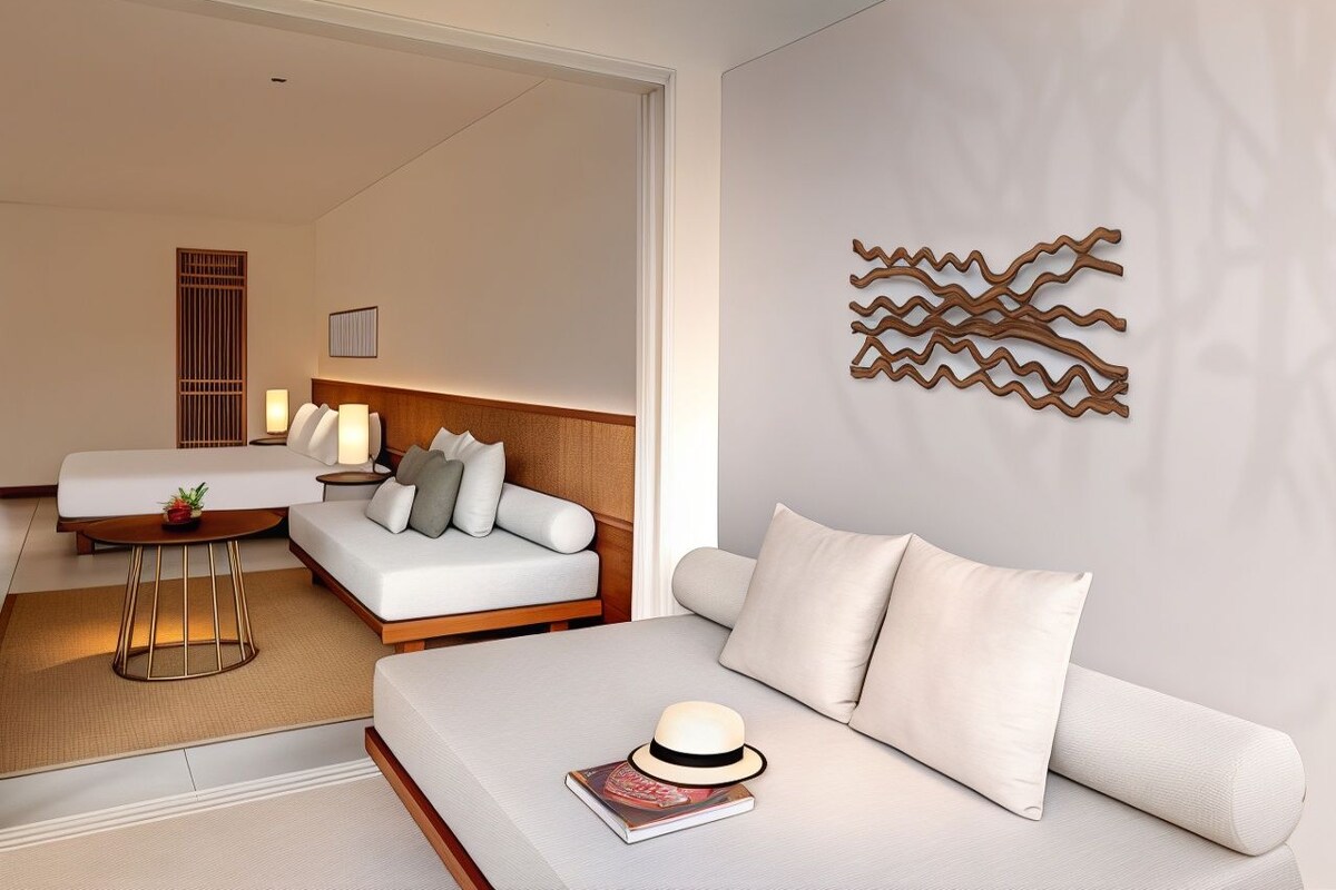Una habitación de hotel moderna con sofá, una mesita, un adorno en la pared y una cama con cabecera.