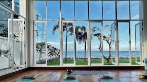 Quarto espaçoso com grandes janelas e vista para o oceano e palmeiras.