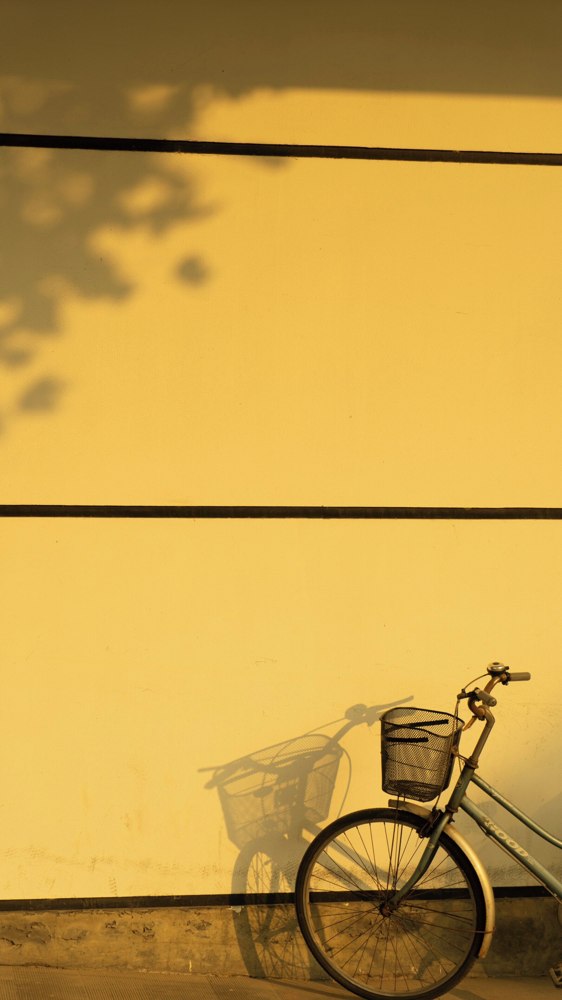 A bicycle with a basket against a yellow wall.