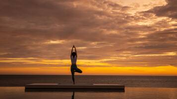A person performing yoga on a platform by the sea during sunset.