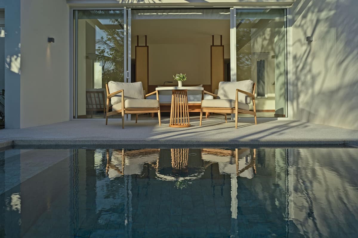 A modern outdoor pool area with a glass door leading to a seating area with two chairs and a small table.