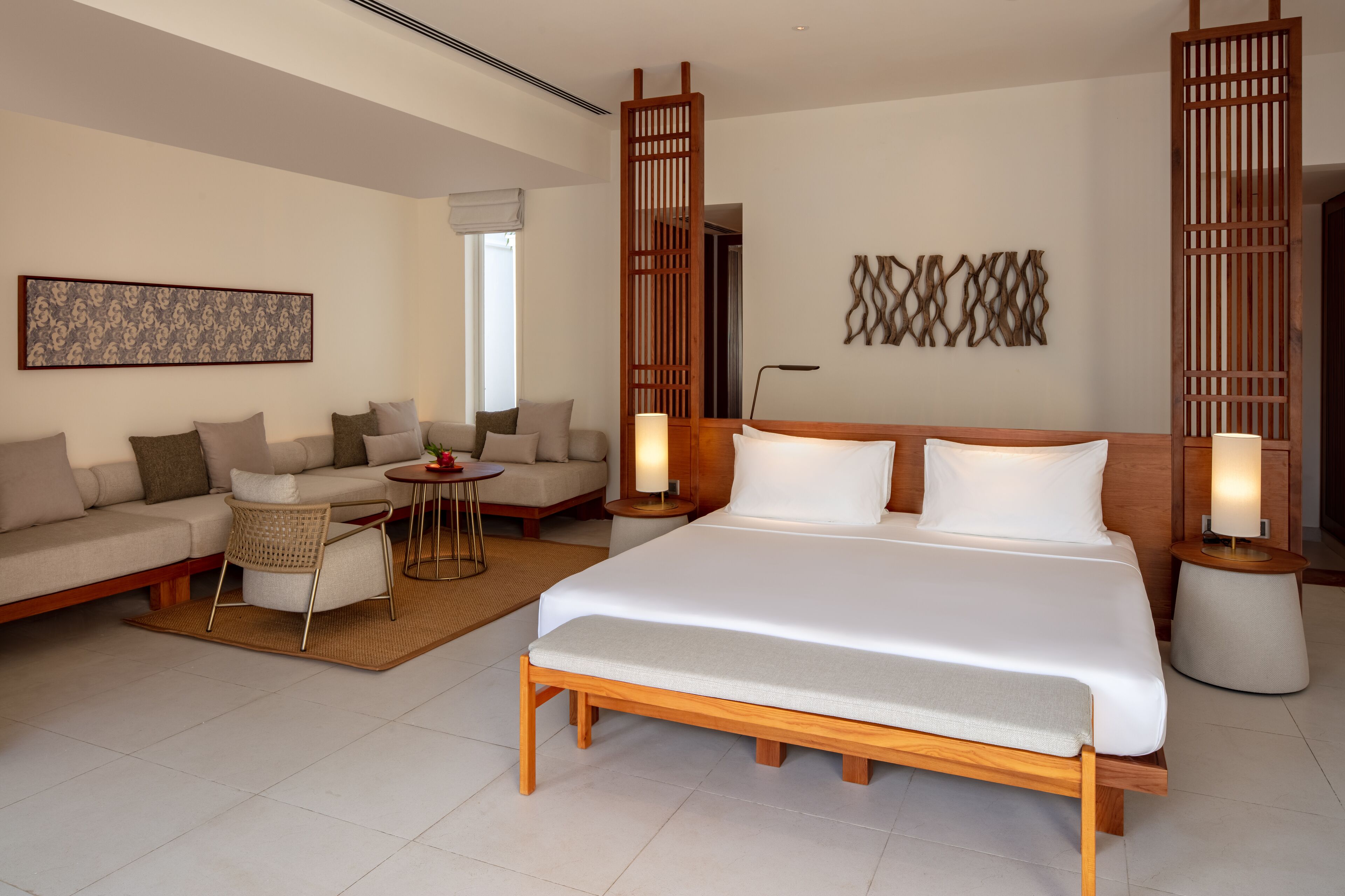 A modern hotel room with a large bed, a sofa, a small table, and decorative wall art.