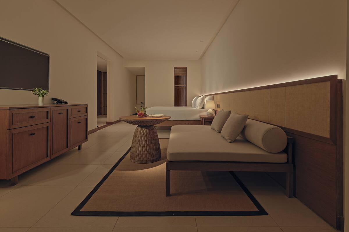 A modern hotel room with a sofa, a small table, a TV, and a bed.