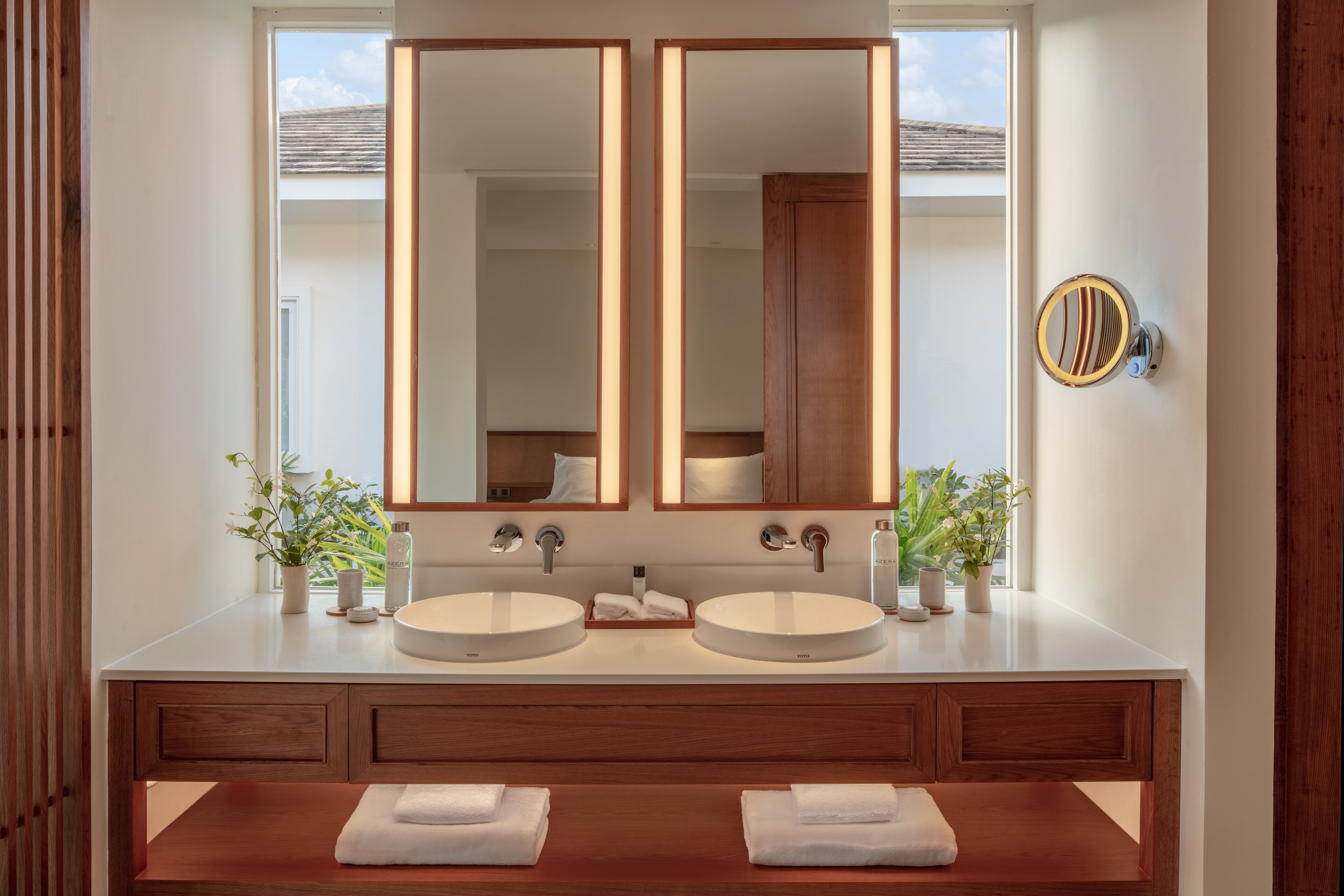 A modern bathroom with two sinks, wooden vanity, large mirrors, and potted plants.
