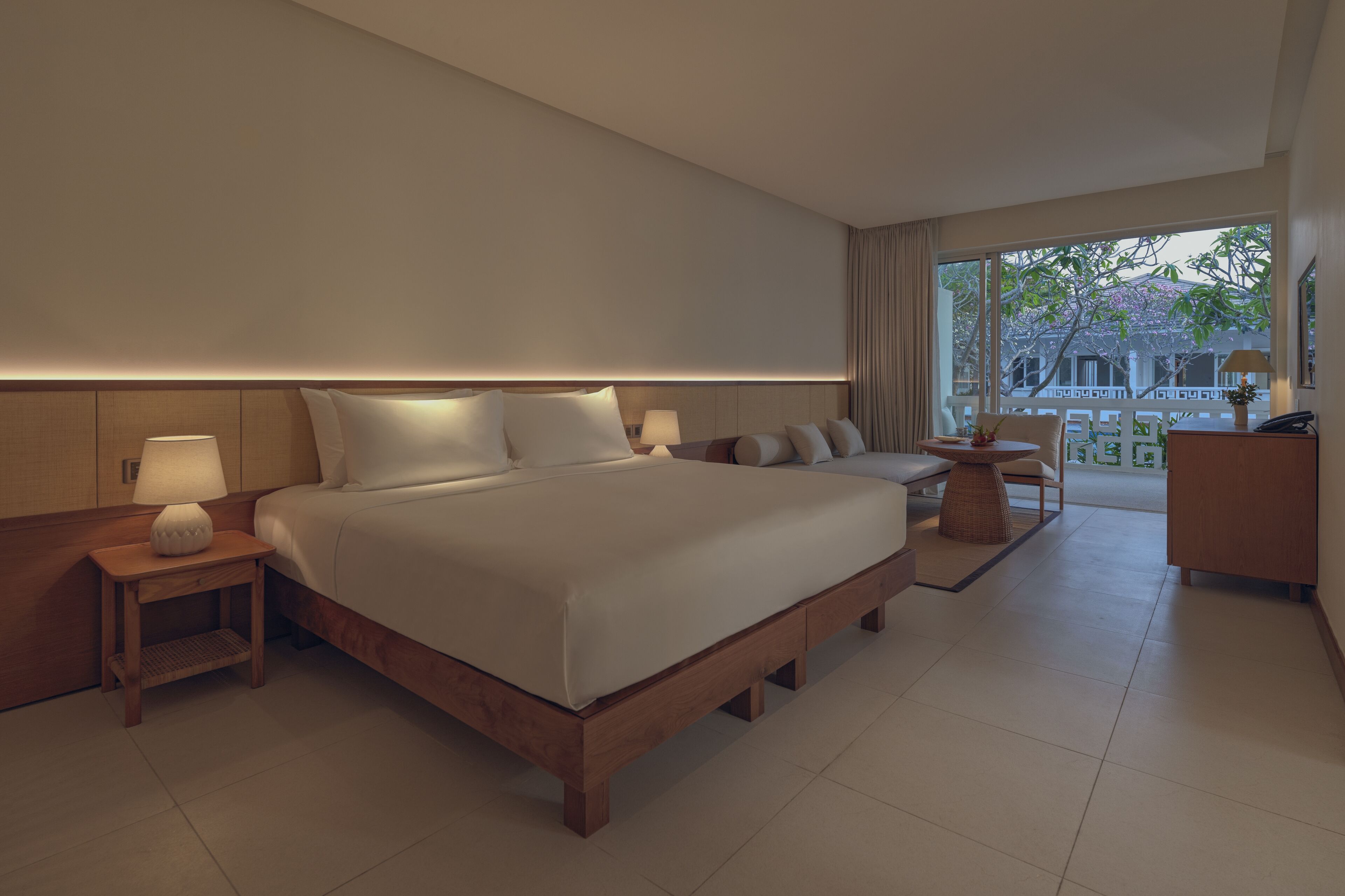 A modern hotel room with a large bed, bedside lamps, a small table, and a view of the outside.