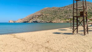 Une plage avec un poste de surveillance pour les sauveteurs, une eau d’un bleu limpide et une colline rocheuse en arrière-plan.