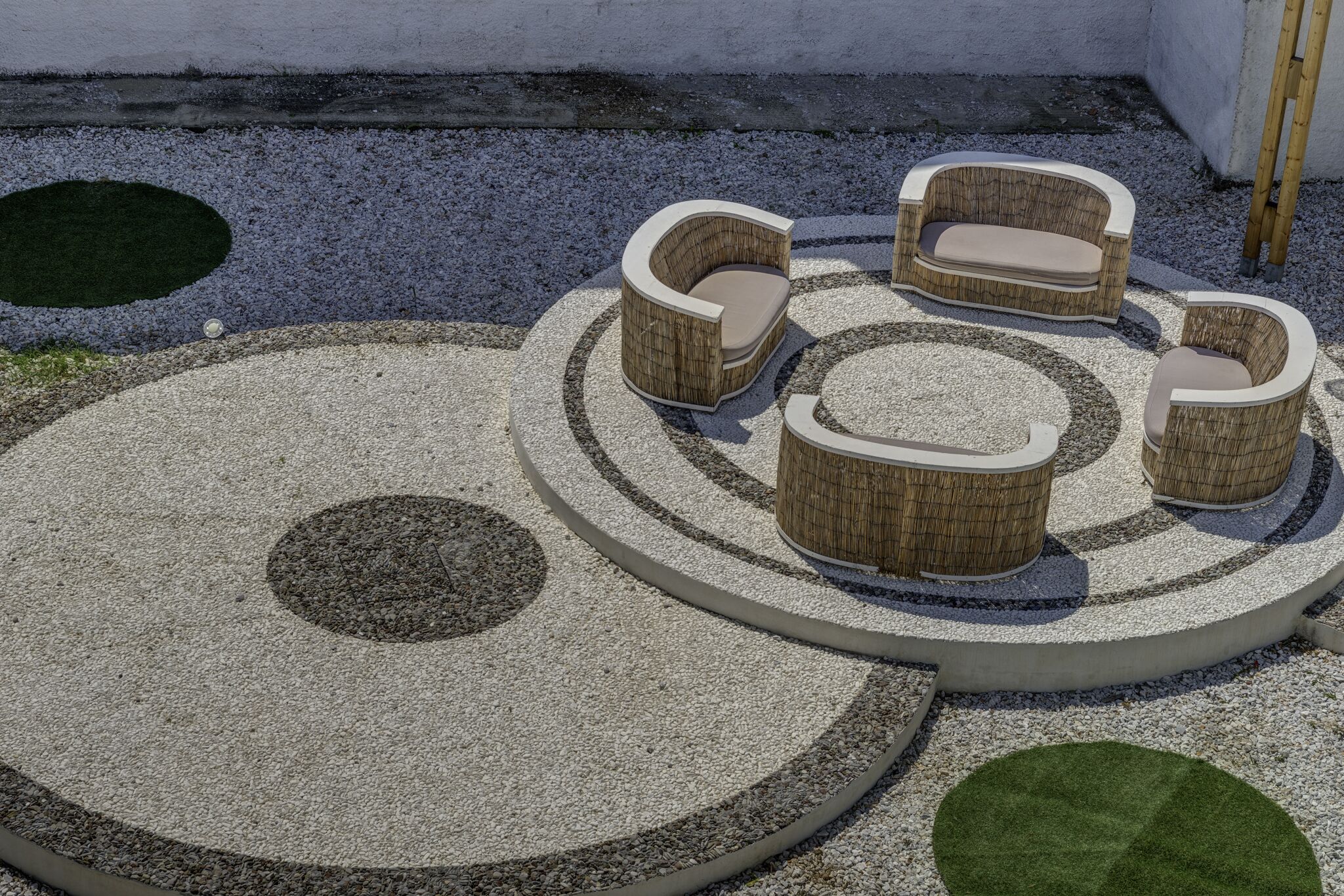 Un espacio de estar al aire libre con forma circular, con cuatro sillas de mimbre y una mesa central, rodeado por una superficie de grava con diseños circulares.