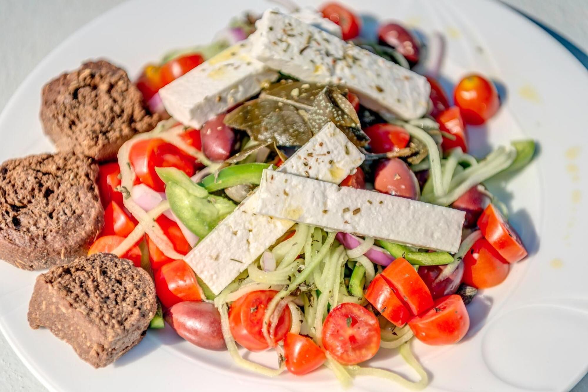Un plato con ensalada, queso feta y pan.