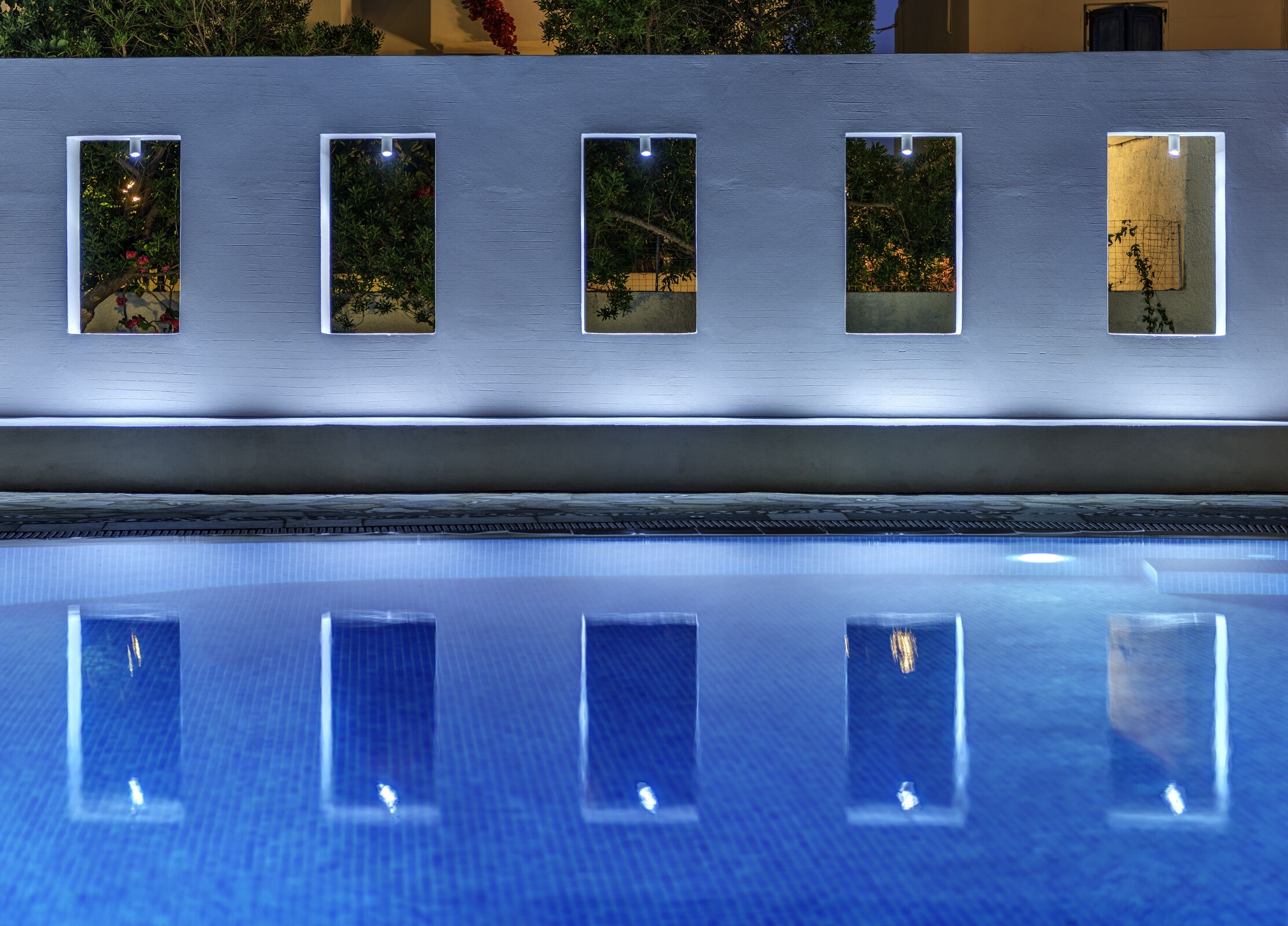 A swimming pool with a series of rectangular windows reflecting the surrounding foliage.
