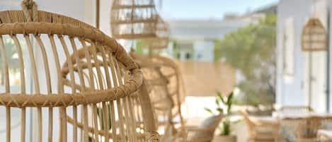 Wicker furniture with a rope hanging from the top, arranged on a balcony with a view of buildings and greenery.