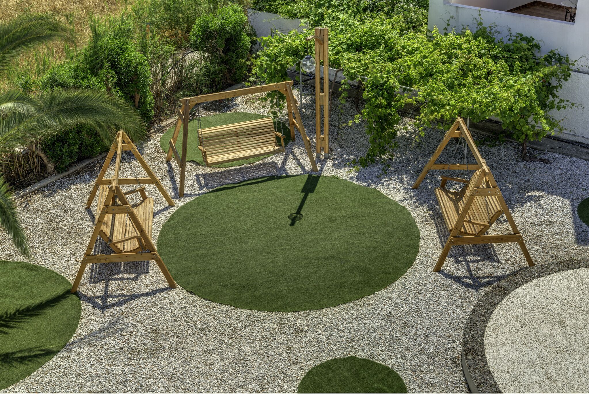 Un jardín con un columpio, un banco y una zona circular verde rodeada de grava.