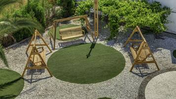 Un jardín con un columpio, un banco y una zona circular verde rodeada de grava.