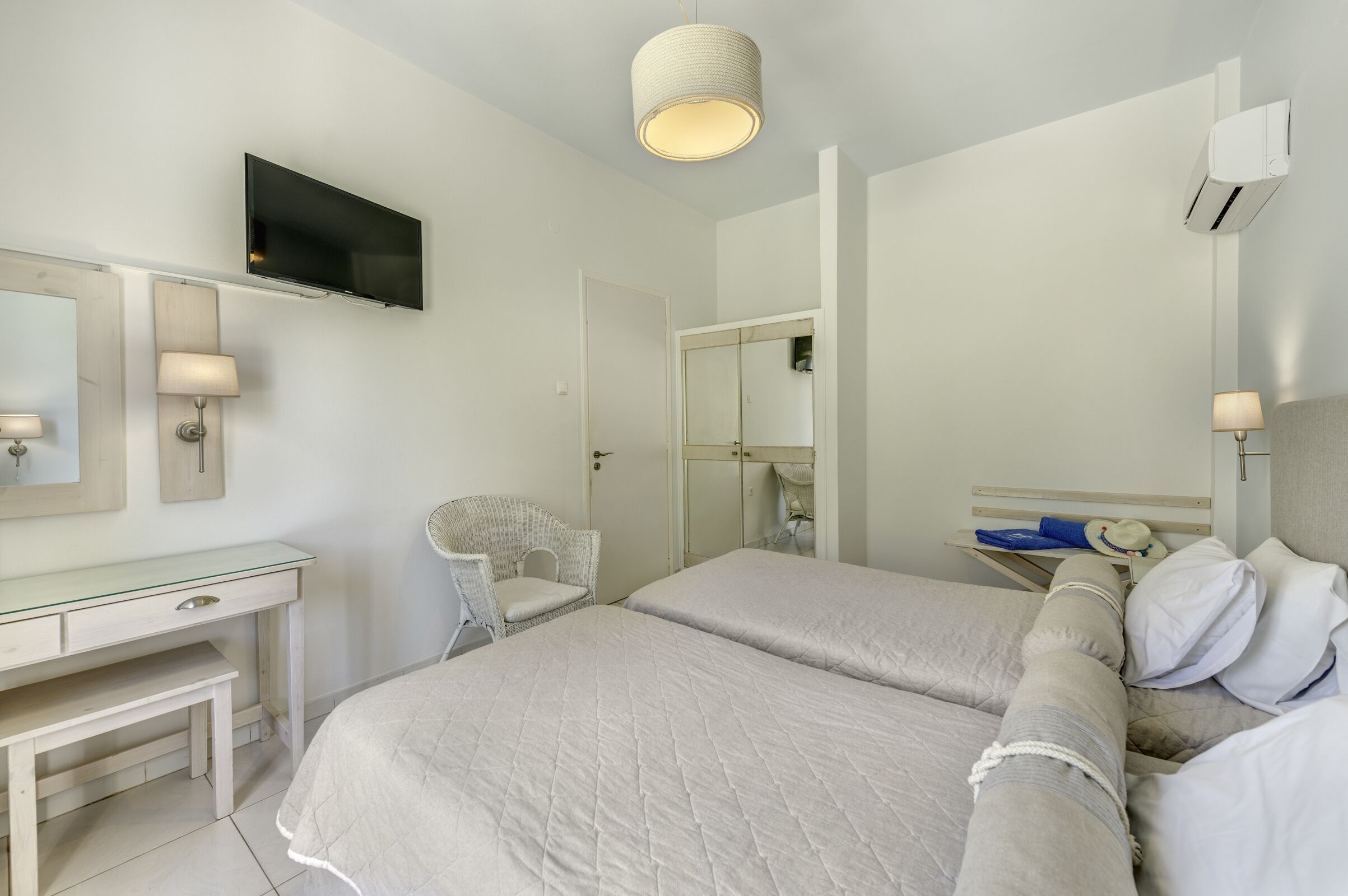 A bedroom with a bed, a desk, a chair, a TV, and a mirror.