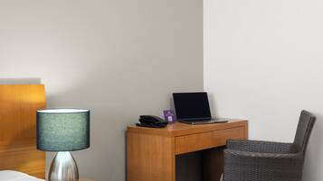 Et hotelværelse med en seng, et skrivebord med en bærbar computer, en telefon og en lampe.