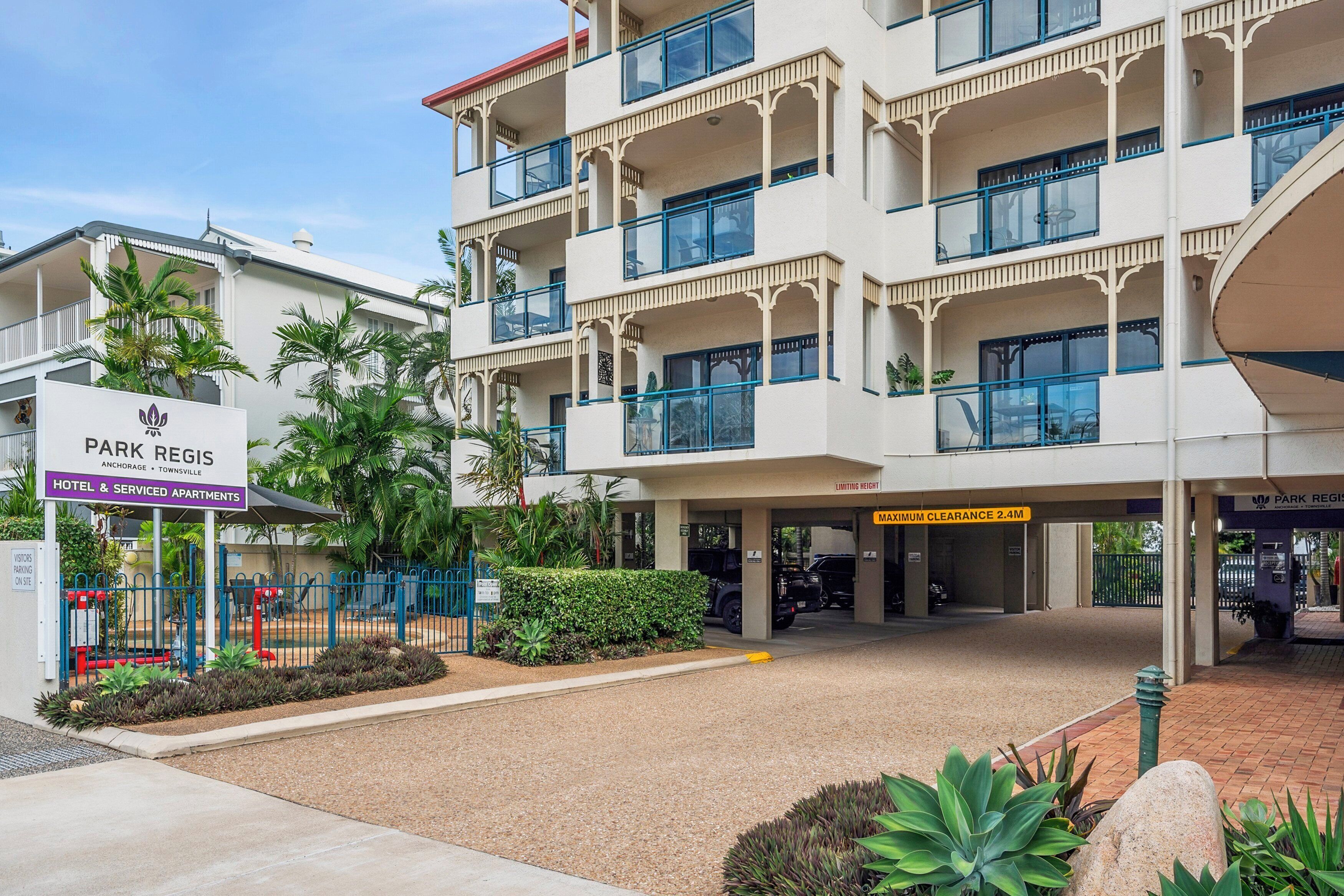 Un hôtel à plusieurs étages doté de balcons, une enseigne indiquant « Park Regis Hotel & Serviced Apartments », et un espace de stationnement avec une signalisation indiquant une hauteur maximale de 2,4 m.