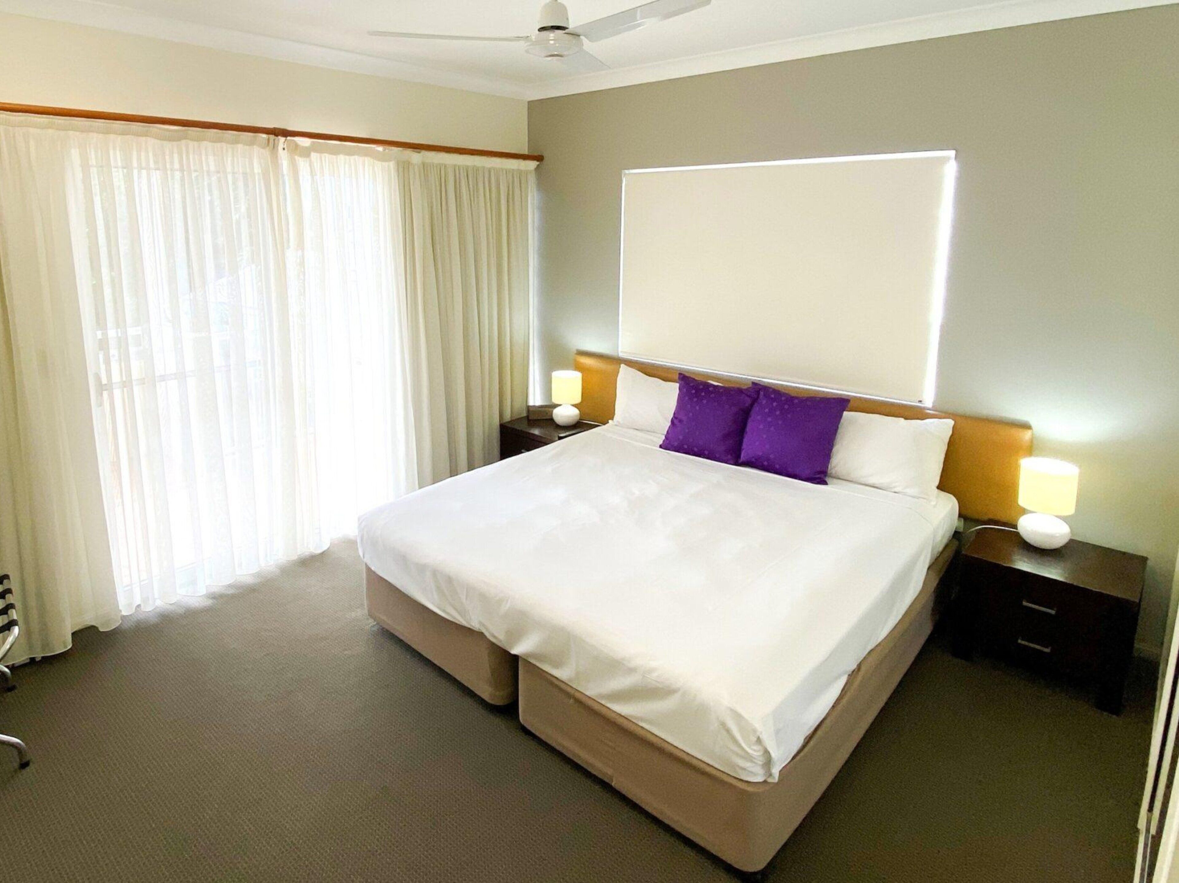 Une chambre d’hôtel avec un grand lit, un ventilateur de plafond, une fenêtre avec des rideaux et des lampes de chevet.