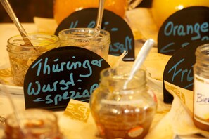 A table with various jars and containers, each labeled with handwritten signs indicating different types of honey. - Adler Golf-& Tagungshotel (Harth-Poellnitz)