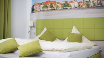 A bed with green and white bedding, a green headboard, and a cityscape mural on the wall behind.