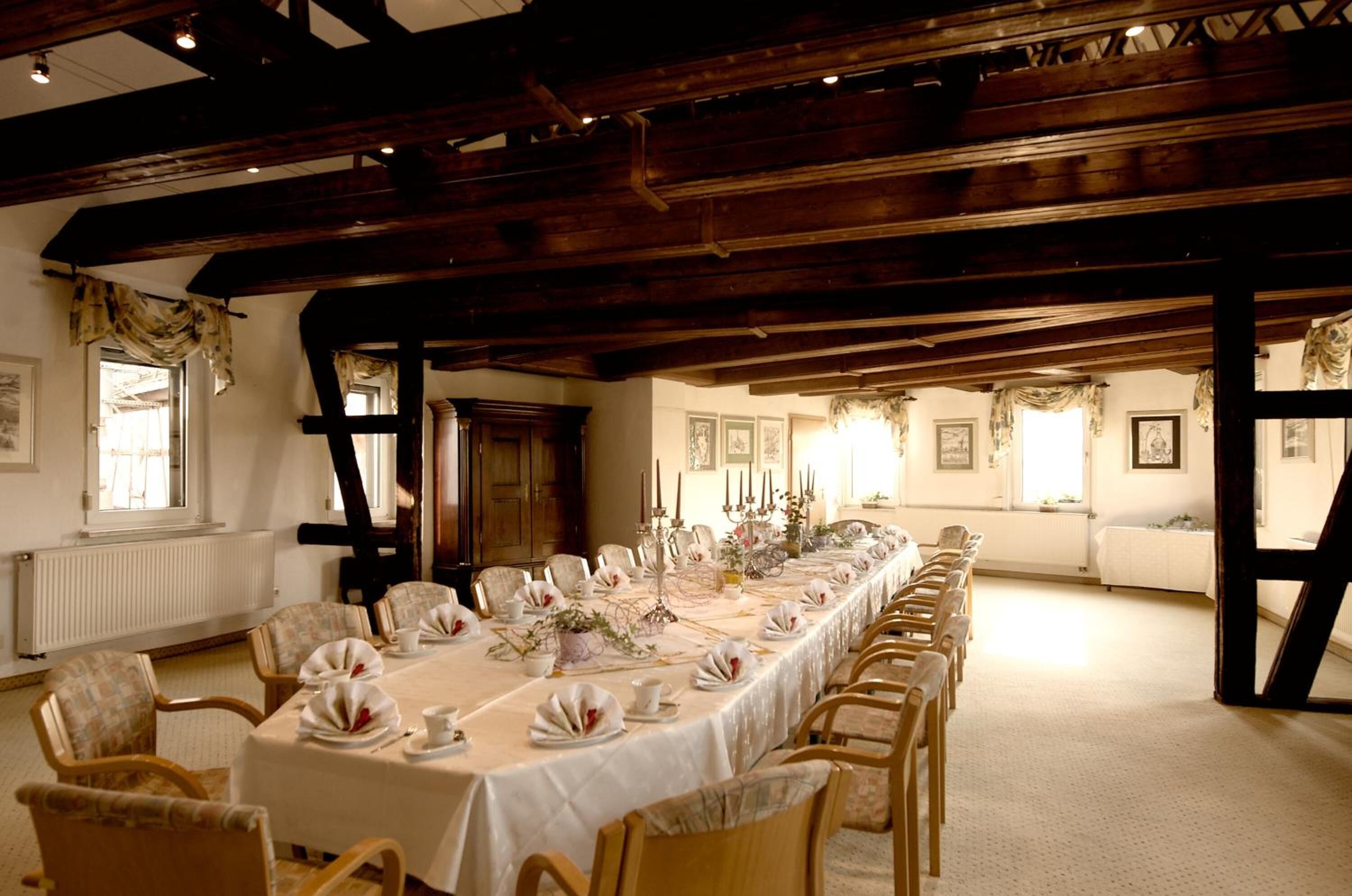 Ein langer Esstisch ist für eine Mahlzeit gedeckt in einem Raum mit freiliegenden Holzbalken und hoher Decke.